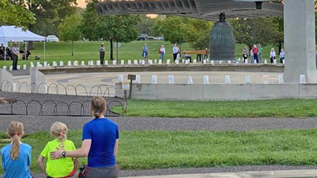 A man and two small children sit on a wall looking toward a large brass bell.