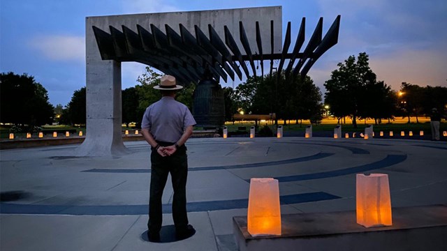 A park ranger stands in front of a large brass bell at dawn.