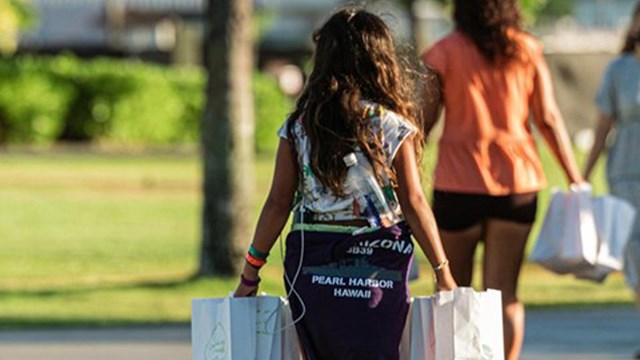 Three women walking in sunlight holding several luminaria bags.