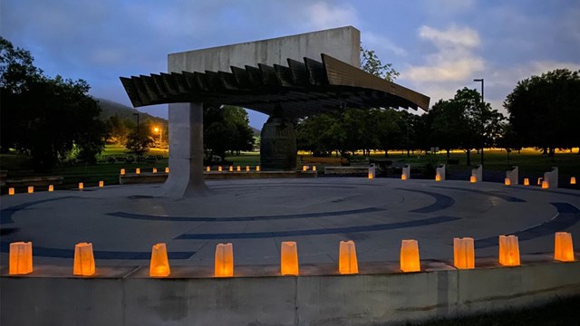 A large brass bell surrounded by luminaria bags at dawn.