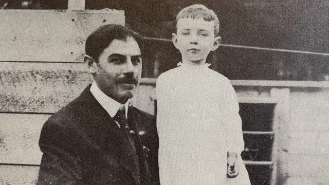 Black and white photo of a seated man with a young boy standing beside him.