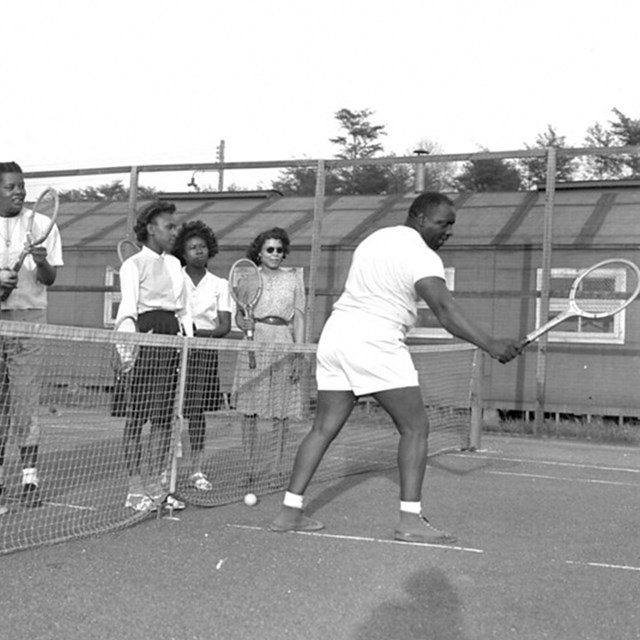 Several men and women playing tennis on an outdoor tennis court.