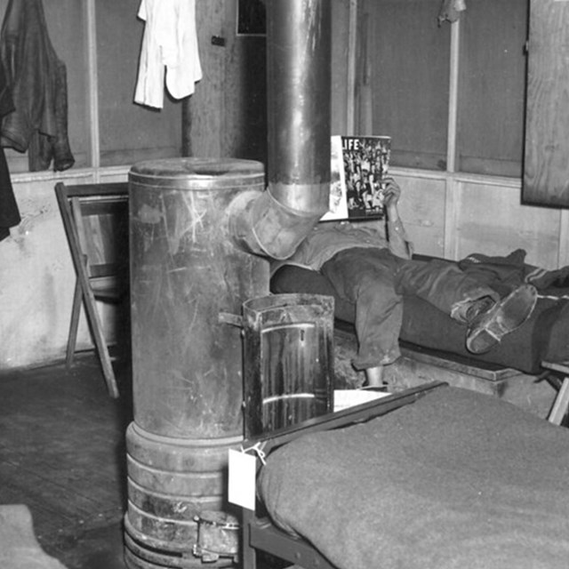 Interior of a small shack with a wood-burning stove at center. 