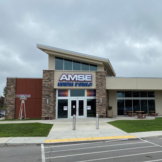 Exterior image of a museum in a strip mall with a sloped roof. The sign o