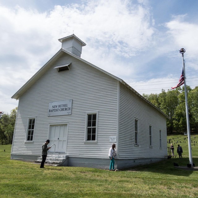  A white wooden church on a grassy hill with a flagpole to the right.