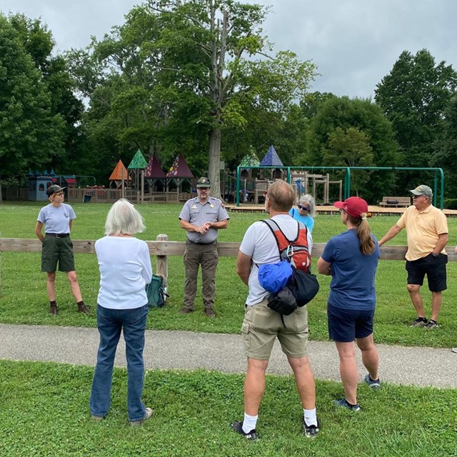 Several people standing around two rangers in a city park.