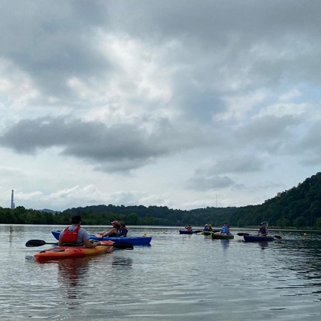Several kayakers on a river. Puffy clouds fill the sky. 