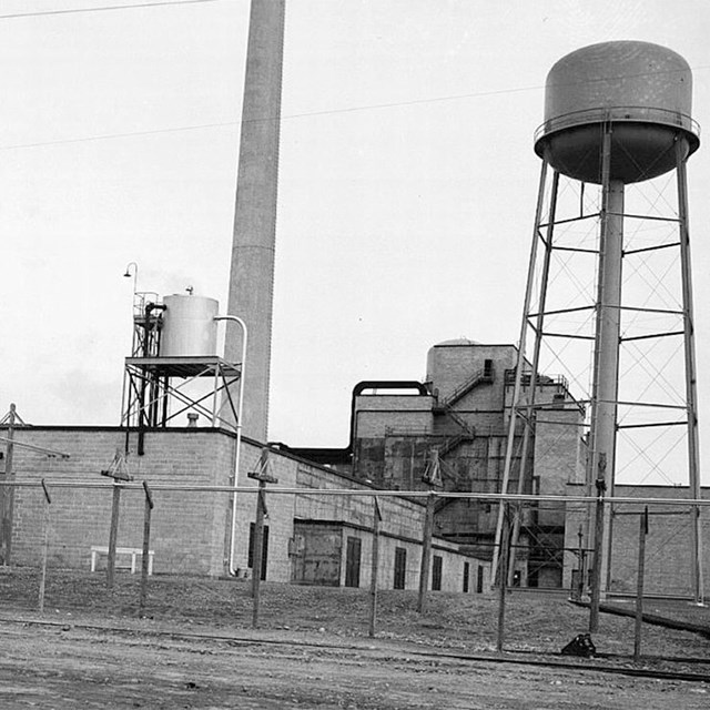 An industrial facility with a water tower and smokestack.