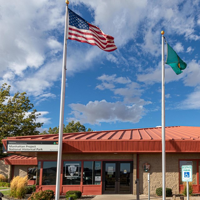 Exterior photo of a building with a rust colored roof. The sky is blue and there are two flags on fl