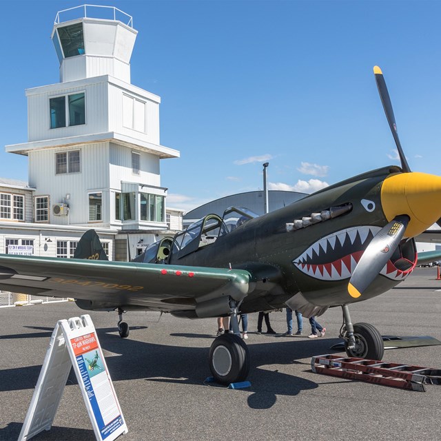  An image of a World War II-era fighter plane on a runway with buildings behind it.