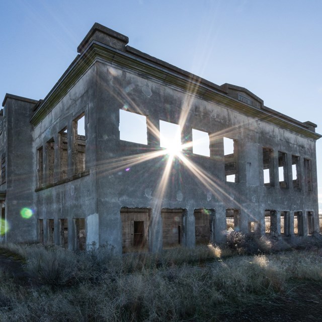 As the sun goes down, it shines through an old gray building with no windows and nothing inside of i