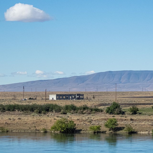 A lone building on a riverbank with mountains in the background.