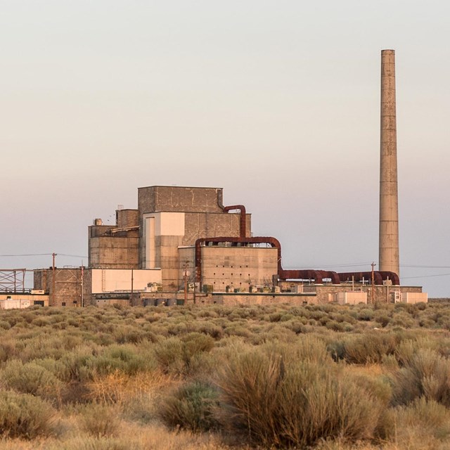A color photo of a blocky building with a ventilation stack in a bushy, treeless field.