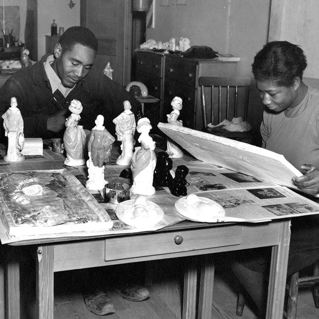 A black and white photo of two people at table. 