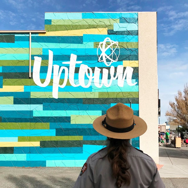 A color photo of a woman in a flat hat standing before a building with the word 