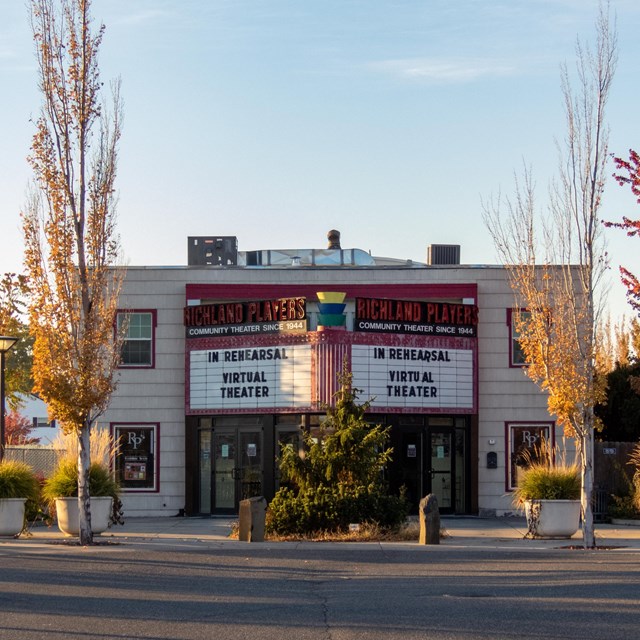 A theater with a large marquee in a parking lot surrounded by trees.