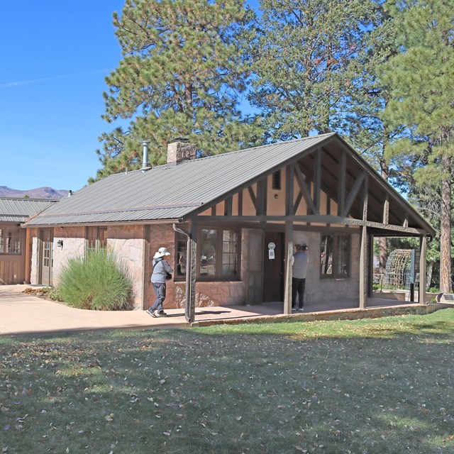 Two people walk into a historical house with a roofed porch.