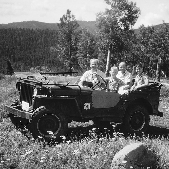A black and white photo of a jeep with an adult and several children.
