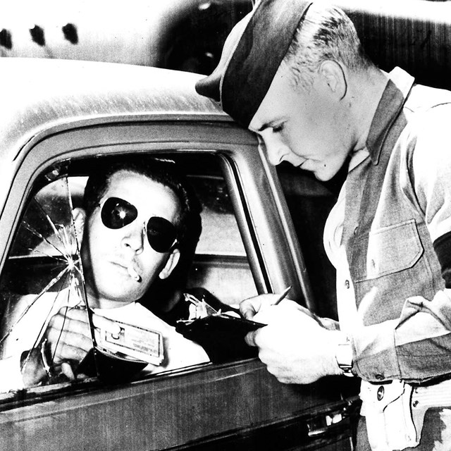 A man checks the badge of another man in a car. 