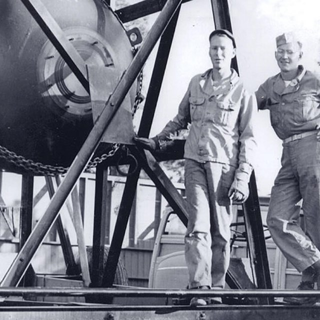 Two men stand next to a large metal orb.