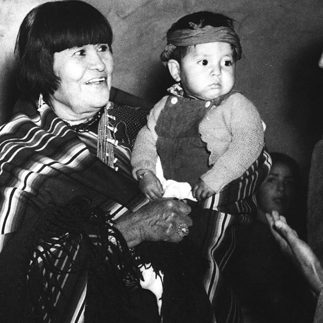 A woman holding a child smiles at a man in a suit.