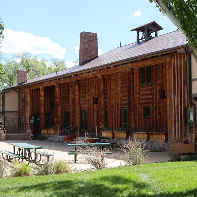 A rustic wooden building surrounded by green grass, trees, picnic
