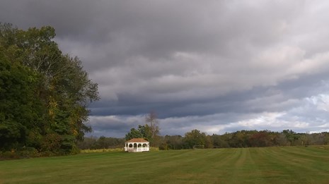 Field with gazebo and farm in the background with a gray sky 
