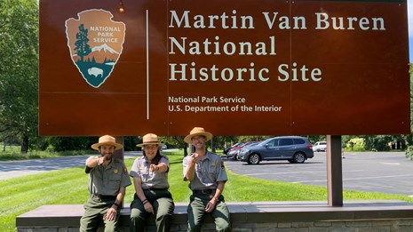 Three Rangers sit in front of the Martin Van Buren National Historic Site entrance sign.