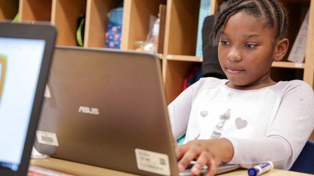 Young student with braids looks at laptop in a classroom