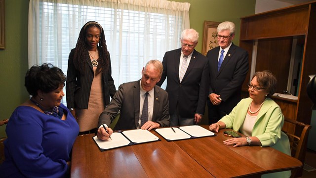 Reena Evers and others gathered around table in Evers Home while Secretary Zinke signs policy