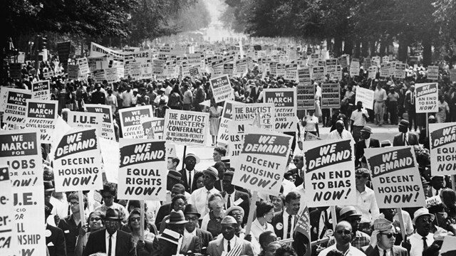 A parade of 1960s civil rights activists marching with signs. 