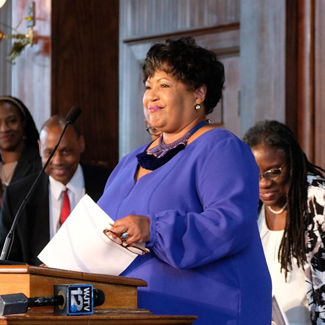 Reena Evers stands at church podium and smiles out to crowd