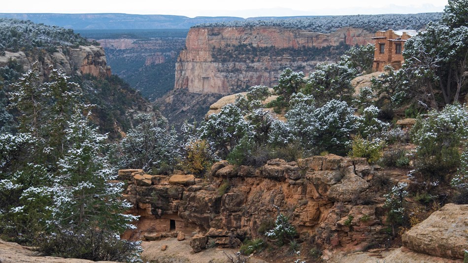 Looking down a snowy canyon, with an ancestral masonry structure in a cliff alcove 