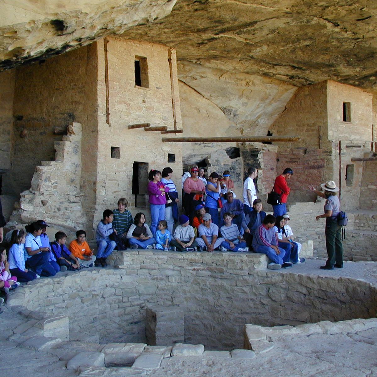Students group around a kiva in a cliff dwellling