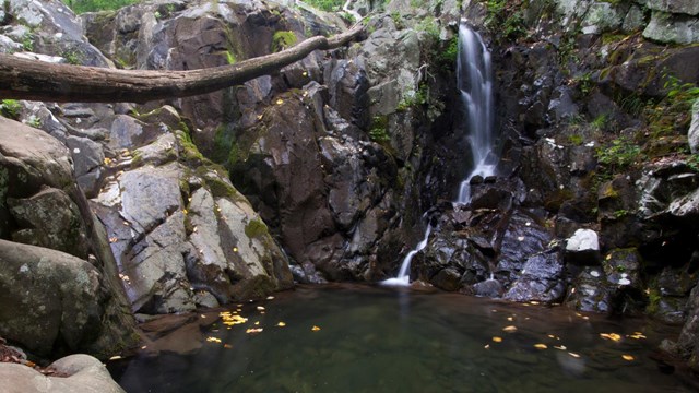 A small waterfall cascades several feet down into a dark turquoise pool