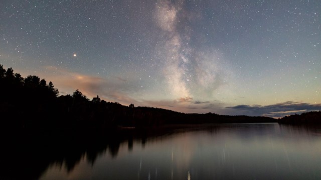 Milky Way over water and the silhouette of trees.