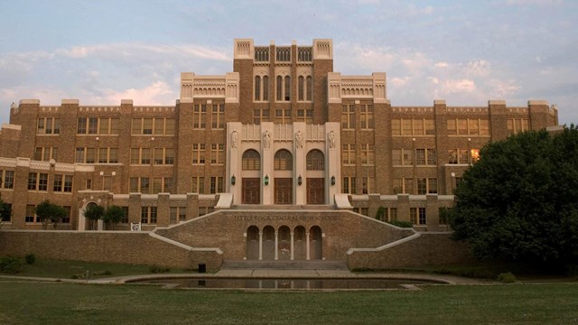 A staircase leads to an elaborate facade of a large brick high school.