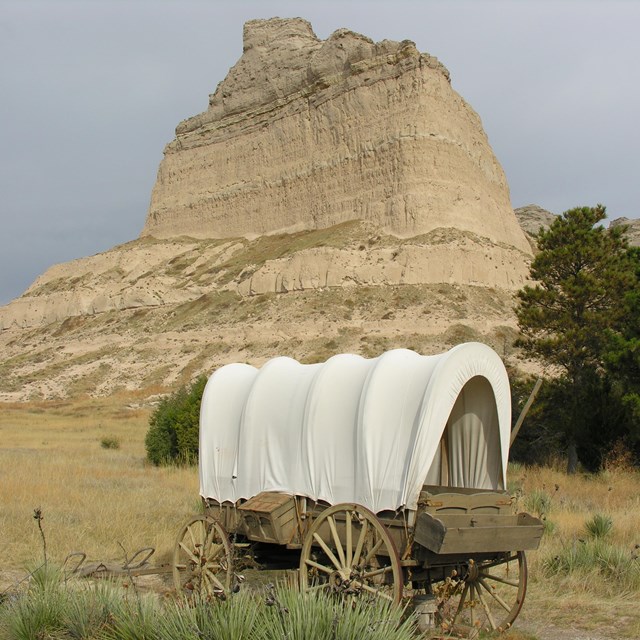 Covered wagon in front of a tall buff. 