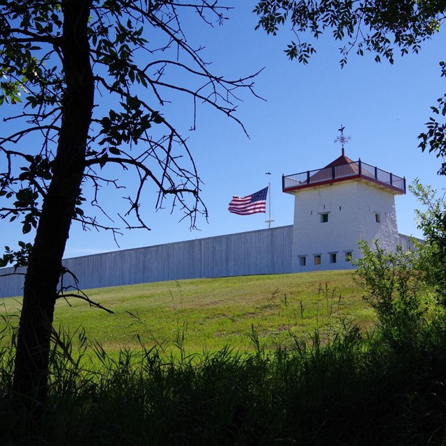 View of a white fort wall and corner tower from below and through trees. 