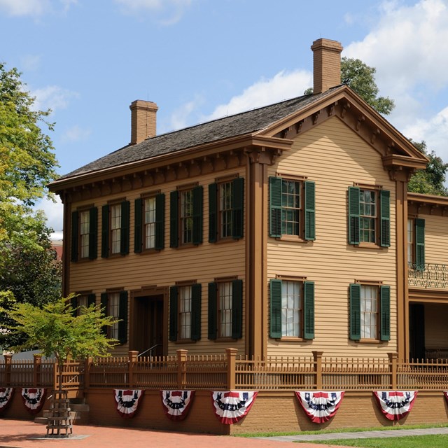 Two story home next to a tree with orange siding and many windows with green trim.