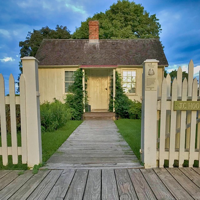 Small one story cottage with a fence and walkway in front. 