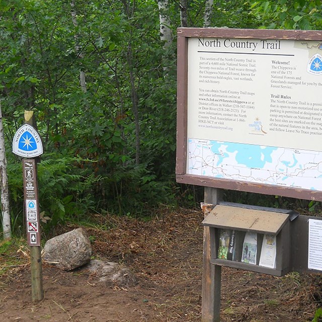 Trailhead in the woods showing an information board and a sign that says 