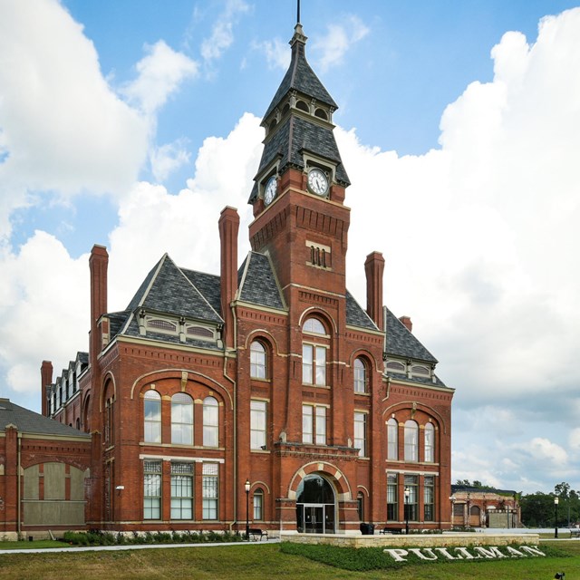 The front of a tall red brick building with a clock tower and many windows. 