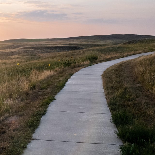 Sunrise sky over softly lit cement sidewalk style hiking trail and rolling hills. 