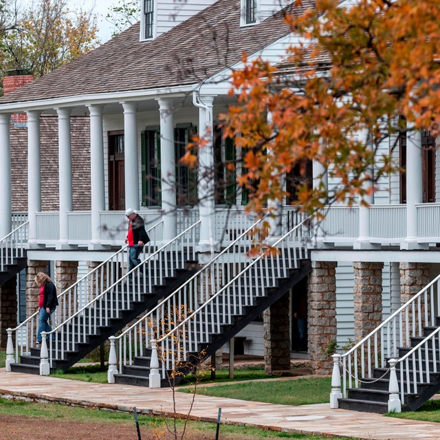 People walking down the stairs of one of two white multi-story buildings. 