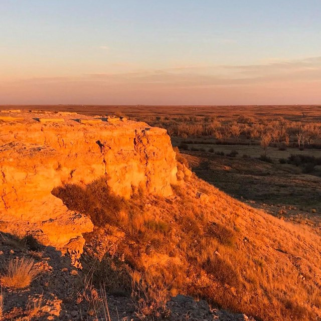 A rocky viewpoint featuring two informational waysides overlooking a rolling grass landscape.