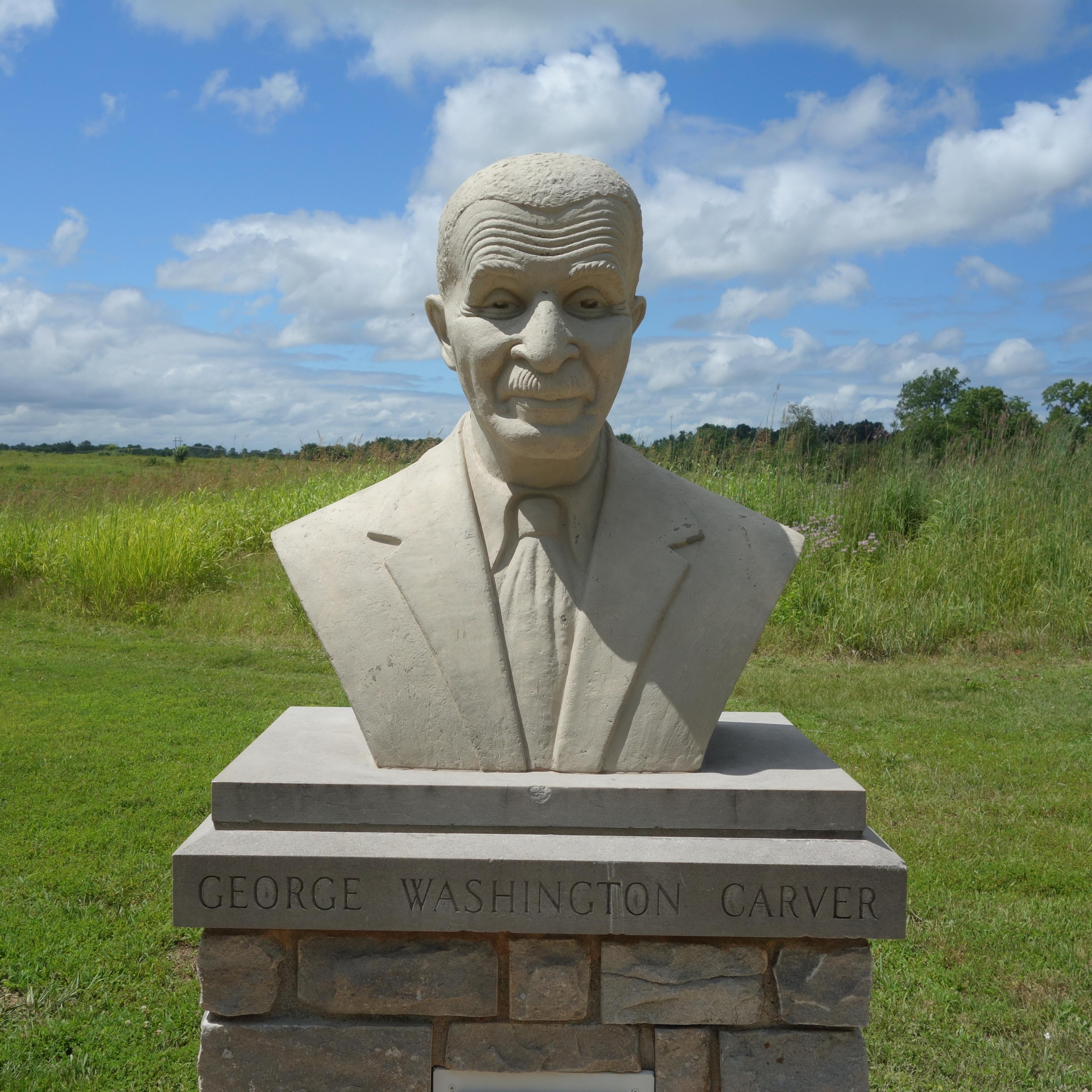 A cast concrete bust of George Washington Carver and prairie in the background.