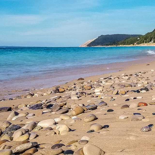 Sand and pebbles in foreground with turquoise water in background.