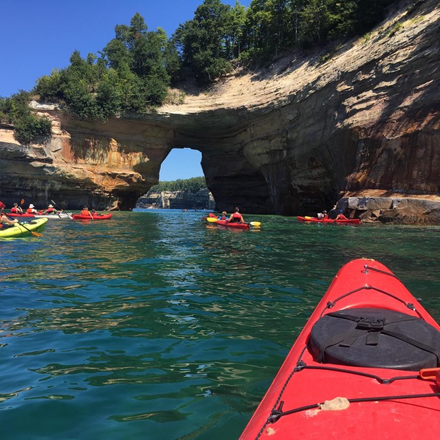 Kayakers on a lake near an arch formation. 