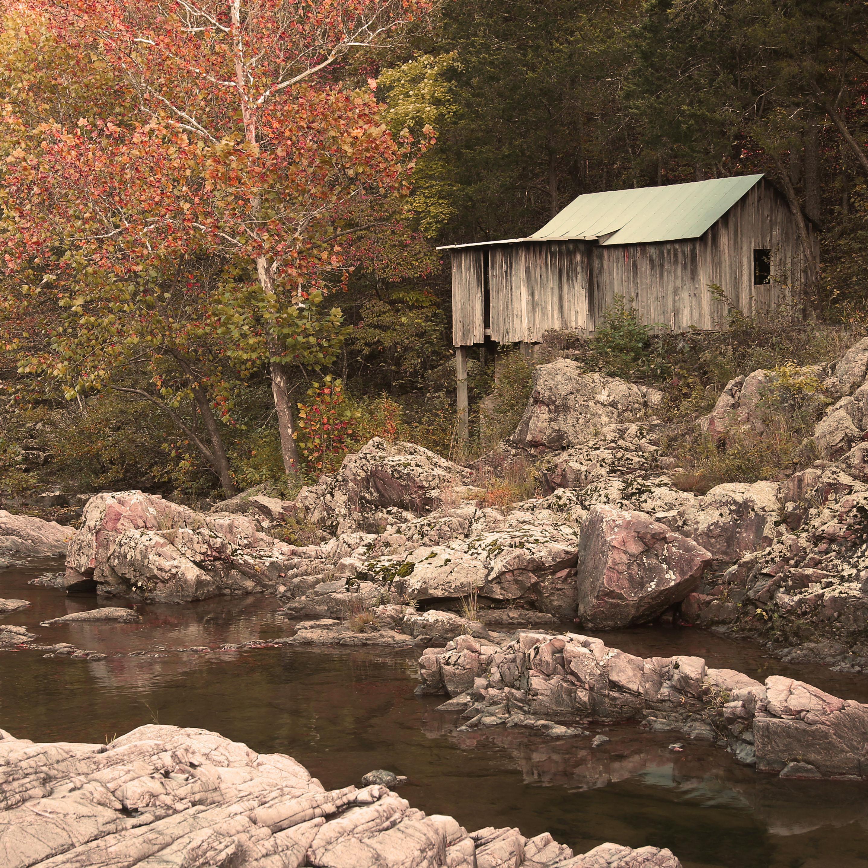 Fall colors on trees surrounding a creek with an old wooden mill on the right.